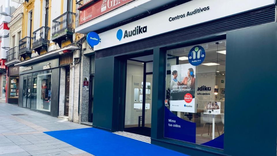 Entrada principal del centro auditivo Audika en Mérida, con fachada moderna y letreros visibles en una calle comercial.