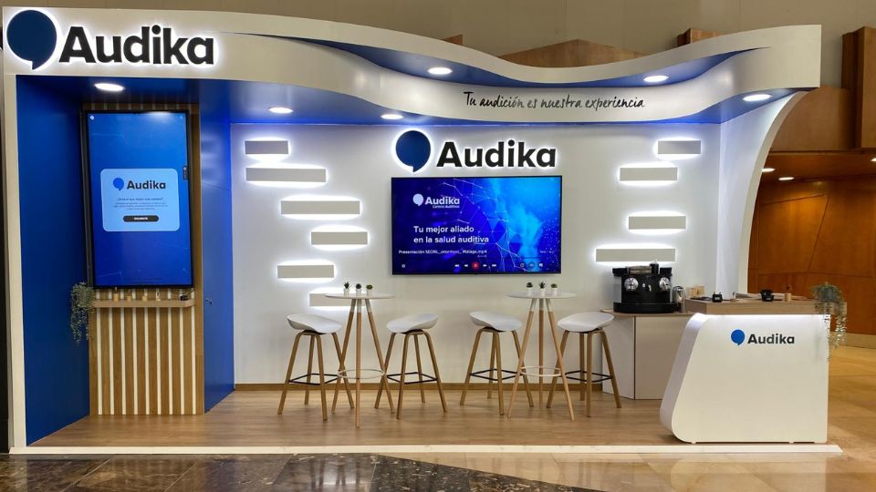 Stand de Audika en el congreso SEORL-CCC con mobiliario moderno, pantalla promocional y área de atención al cliente.