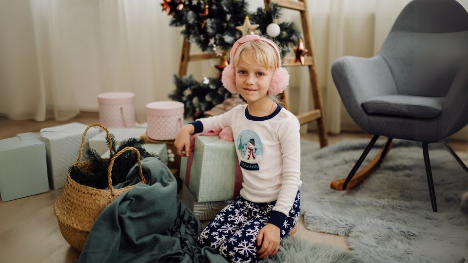 niña sentada junto a regalos navideños y árbol de Navidad decorado