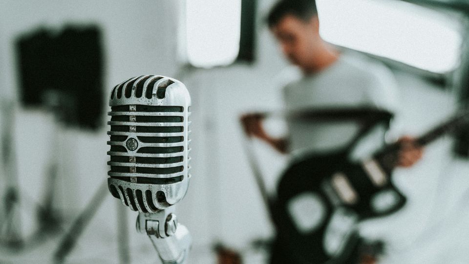 Micrófono antiguo en primer plano con un músico tocando la guitarra en el fondo desenfocado.