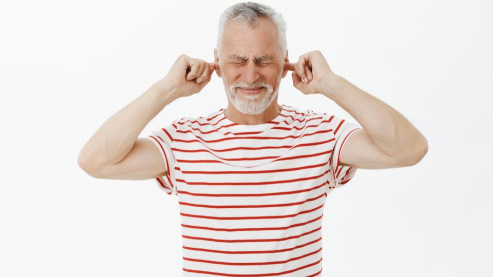 Hombre mayor con molestias en los oídos y dedos tapándolos.