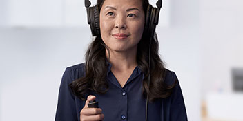 Una persona con audífonos grandes sostiene un control en la mano, realizando posiblemente una prueba de audición en un entorno clínico minimalista asociado a cuidados auditivos. No se observa texto visible.