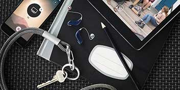 Audífonos con diseño discreto descansan sobre un cuaderno junto a un lápiz, llaves y un dispositivo móvil mostrando una app, en un espacio moderno. Contexto asociado a Audika.