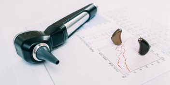 Herramientas de cuidado auditivo, incluyendo un otoscopio y audífonos, colocadas sobre un audiograma con gráficos de resultados.