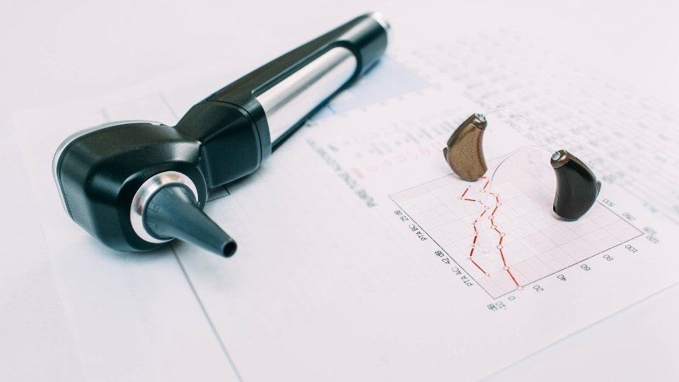 audiograma con dos audífonos y un otoscopio sobre una hoja impresa