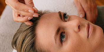 Manos colocan un audífono detrás de una oreja con cabello canoso, en un entorno de clínica auditiva. Contexto cálido y profesional, promoviendo el cuidado de la salud auditiva.