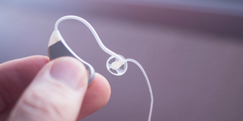 audífono moderno sostenido entre los dedos, destacando la diferencia entre audífonos y amplificadores auditivos