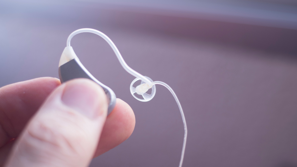 audífono pequeño sostenido entre los dedos de una mano