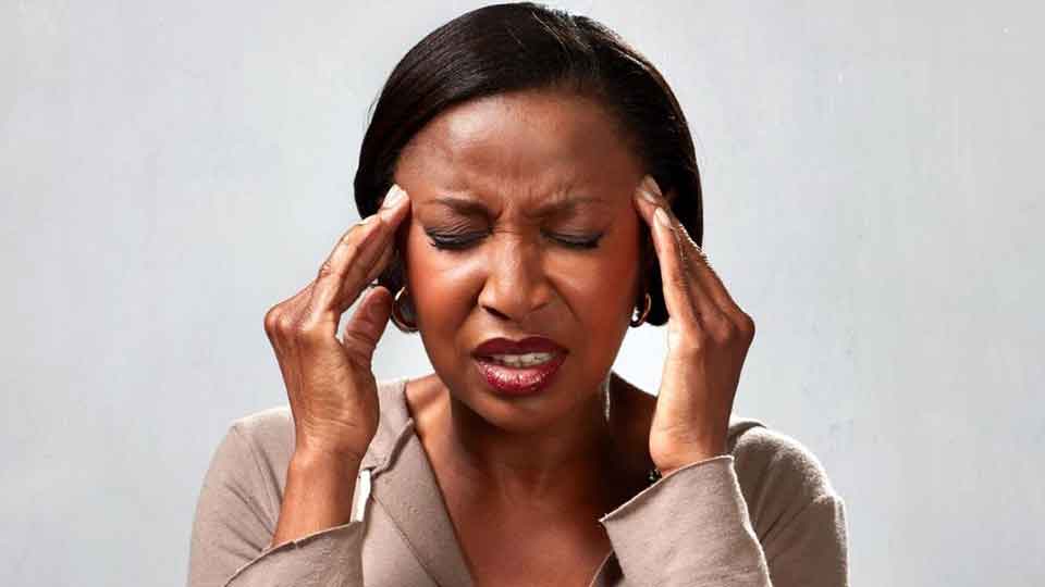 Una persona con manos en las sienes sugiere malestar, posiblemente asociado con problemas auditivos o tinnitus. Fondo gris liso destaca al sujeto, contexto de cuidado auditivo o clínica especializada.