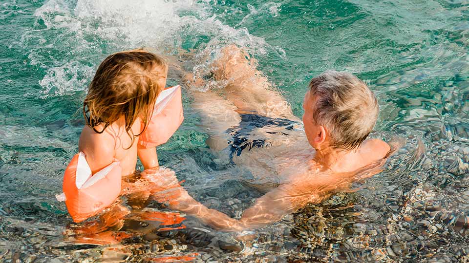 niña con flotadores jugando en la piscina junto a un hombre mayor