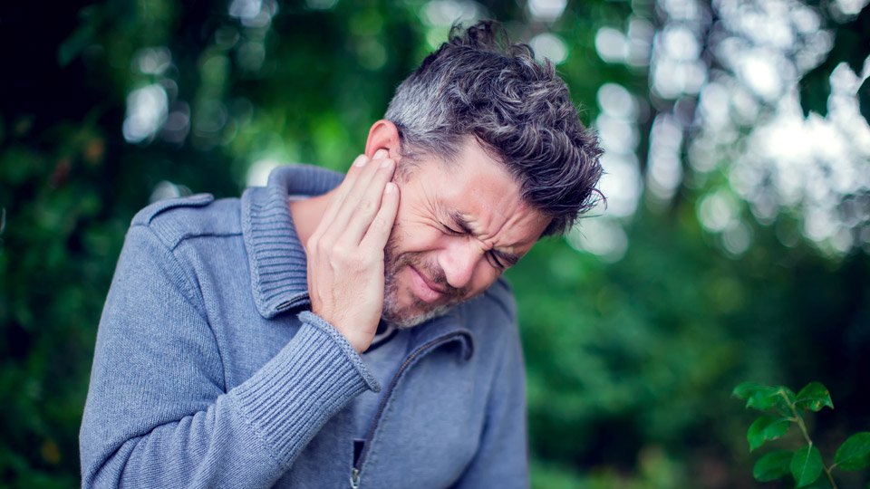 hombre con dolor de oído debido a tinnitus en un entorno al aire libre