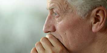 Una oreja humana aparece enfocada, posiblemente de una persona mayor. El contexto es un fondo difuminado verde y blanco. No se observan audífonos ni texto visible en la imagen.