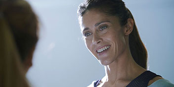 Una mujer con el rostro desenfocado aparece de perfil y cabello recogido, posiblemente interactuando con otra persona en un ambiente iluminado, ideal para un contexto de clínica auditiva o consulta.