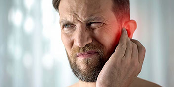 Un hombre toca su oreja derecha, que está resaltada con un brillo rojo simulando dolor. El fondo es difuso, con tonos claros, posiblemente en una clínica auditiva.