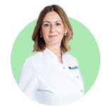 Una profesional de la salud auditiva con bata blanca que lleva el logotipo de Audika en el pecho; fondo verde circular enfatiza su figura, resaltando su rol en un entorno clínico.