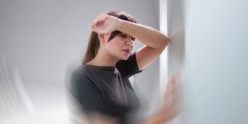 Persona con sensación de vértigo y pérdida de equilibrio, apoyándose en la pared, síntoma frecuente del nistagmo vestibular.