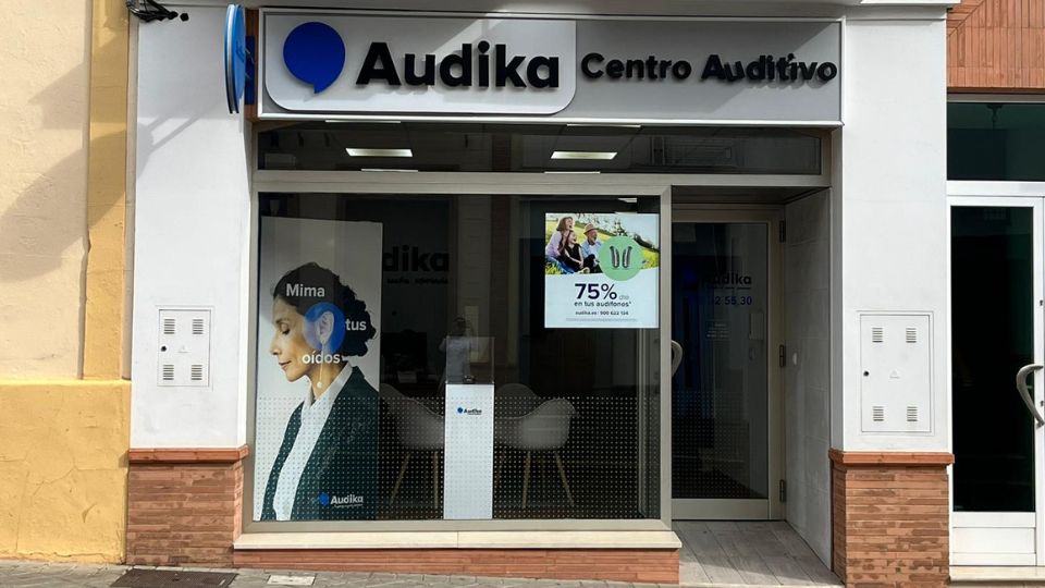 Fachada de un centro auditivo Audika con un letrero que dice 'Audika Centro Auditivo.' En el escaparate, cartel: 'Mima tus oídos' y otro promocional: '75% en tus audífonos.'