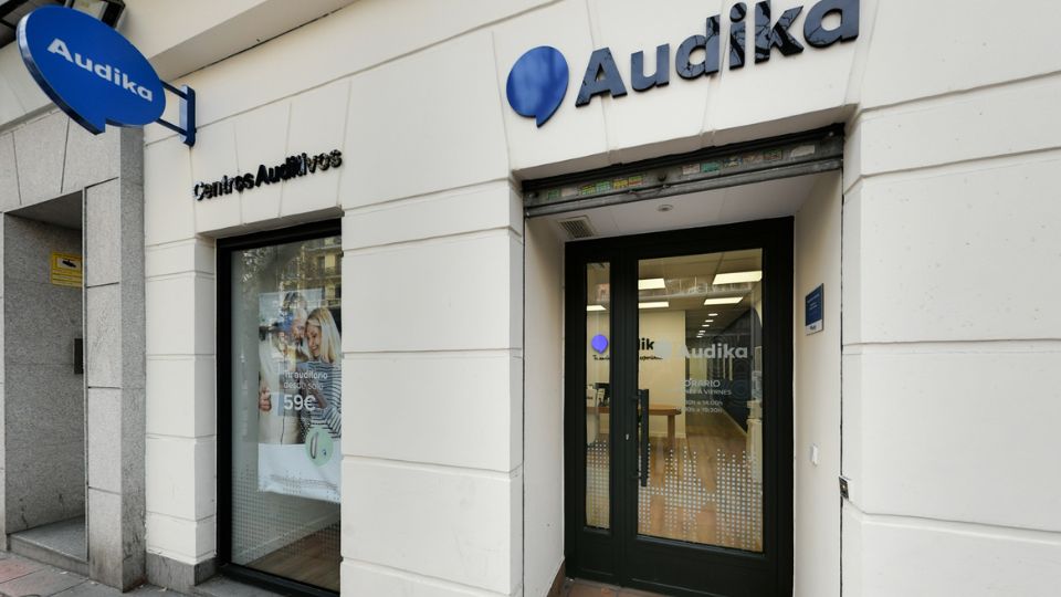 Fachada de una clínica auditiva Audika con letreros que dicen 'Centros Auditivos' y 'Tu salud auditiva importa.' En el escaparate, un cartel promociona audífonos desde 59€.