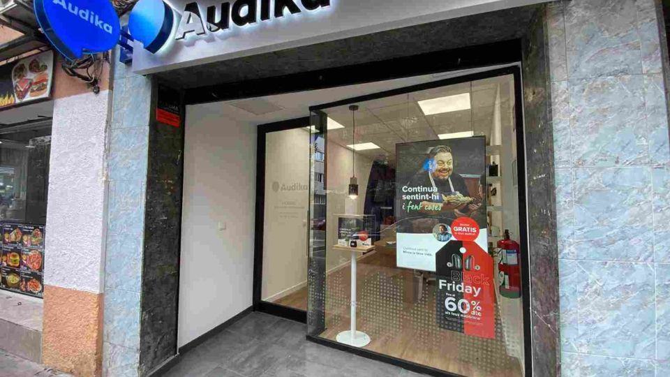 Una clínica Audika presenta su entrada con cristalera; un cartel promociona ’Black Friday: 60% de descuento’ y ’continua sentint-hi i fent coses’. El interior muestra un espacio minimalista.