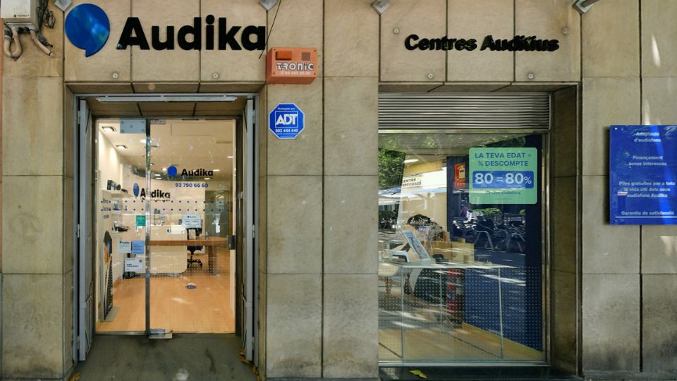 La fachada de un centro auditivo Audika muestra su logo y número de contacto ’93 790 66 69’. Al lado, un escaparate anuncia: ’LA TEVA EDAT = % DESCOMPTE 80 = 80%’.
