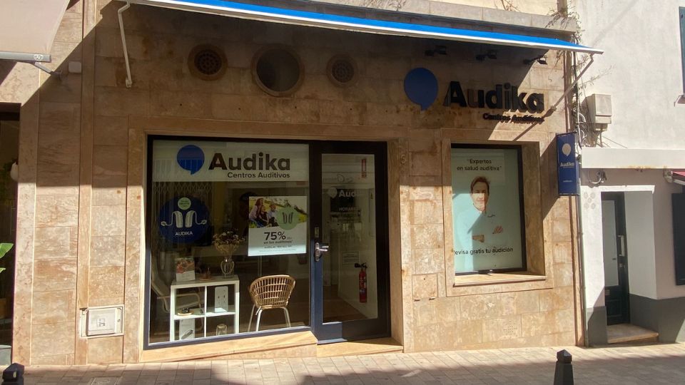 Fachada de una clínica auditiva de Audika, con letreros promocionales en las ventanas que destacan audífonos y oferta del 75%. El local tiene un diseño moderno en un entorno urbano.