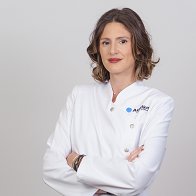 Victoria Candel, audioprotesista en Audika Orihuela, con bata blanca y brazos cruzados.