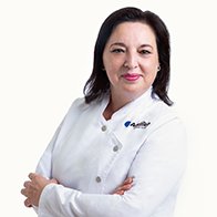 Audioprotesista en Audika Elche, Aurora Cuenca, con uniforme profesional y brazos cruzados.