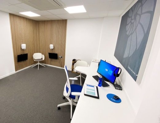 sala de audiometría moderna con computadora, auriculares y panel de madera en pared
