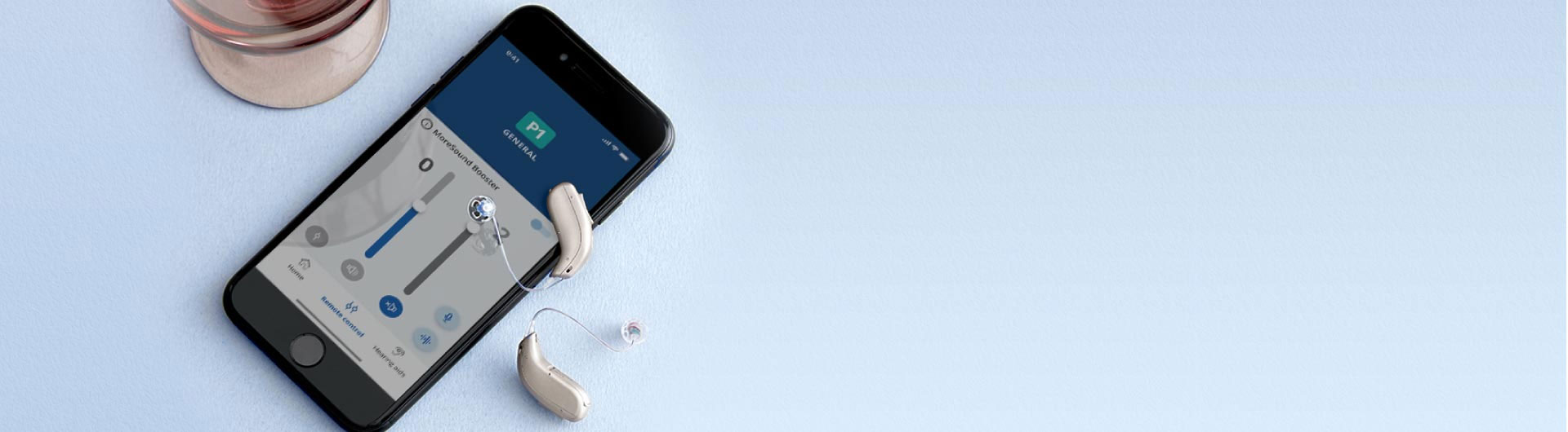 Dos audífonos beige descansan junto a un smartphone que muestra una aplicación de ajustes de sonido, con texto visible: ’P1 GENERAL’ y ’MoreSound Booster.’ Fondo azul claro.