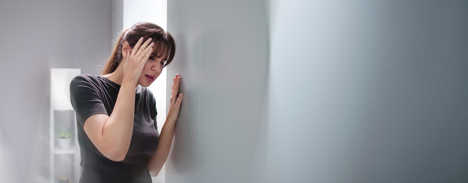 Persona con sensación de vértigo y pérdida de equilibrio, apoyándose en la pared, síntoma frecuente del nistagmo vestibular.