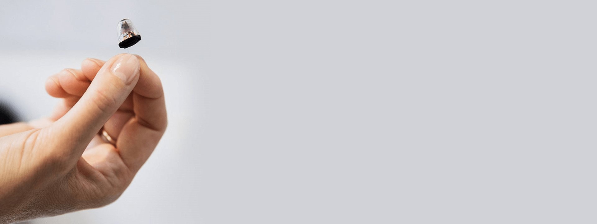 Una mano sostiene un audífono intraauricular Audika discreto, ideal para pérdida auditiva, en un fondo minimalista gris.