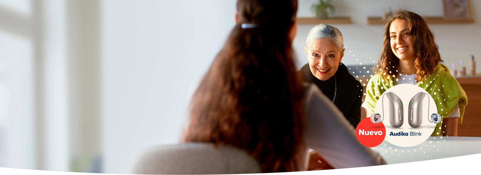 mujer con cabello rizado asesorando a una señora mayor y su nieta sobre audífonos Audika Blink nuevos