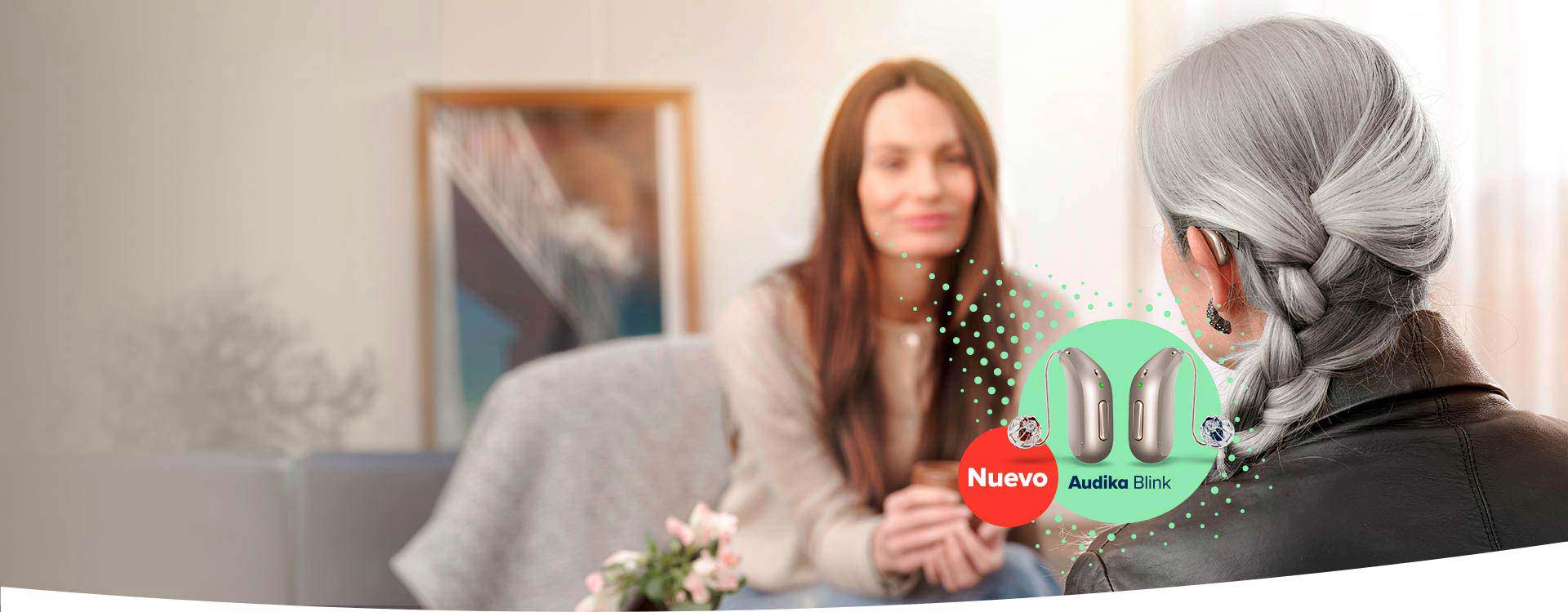 mujer mayor con cabello gris probando el audífono Audika Blink mientras conversa con una mujer joven