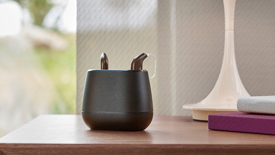 audífonos recargables Audika en su cargador sobre una mesa de madera