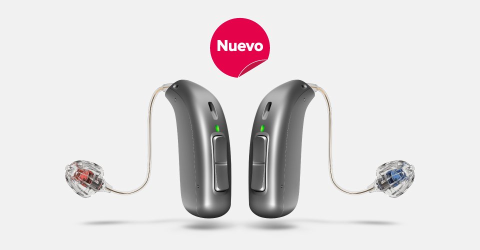 Dos audífonos de tecnología avanzada en gris metálico con moldes intrauditivos en rojo y azul; uno orientado hacia la izquierda y otro hacia la derecha. Fondo blanco. Encima, el texto “Nuevo’ aparece dentro de un círculo rosa.