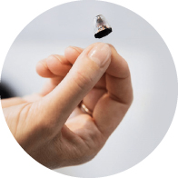 Una mano sostiene delicadamente un audífono pequeño y discreto en un fondo neutro y claro, ilustrando tecnología avanzada en asistencia auditiva, ideal para clínicas auditivas y audiología especializada.