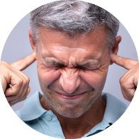 Una persona de cabello canoso apunta con ambos dedos índices a sus oídos, sugiriendo problemas auditivos. Fondo neutro.