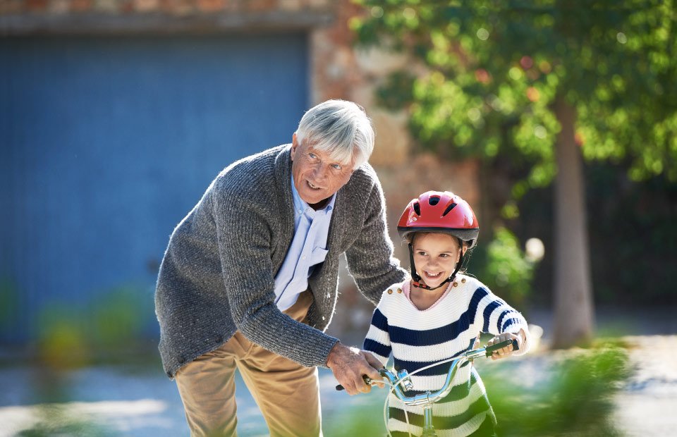 abuelo con audífonos enseñando a su nieta a montar en bicicleta