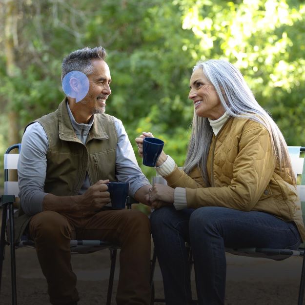 Pareja mayor disfrutando de una conversación al aire libre con audífonos Audika.