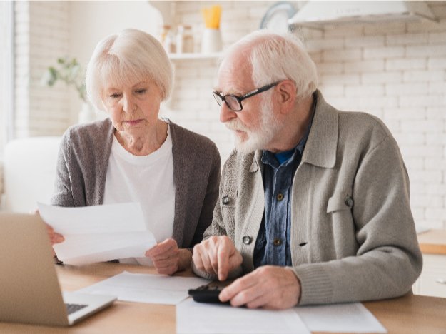 Hombre y mujer mayores revisando documentos en una mesa junto a una computadora portátil.