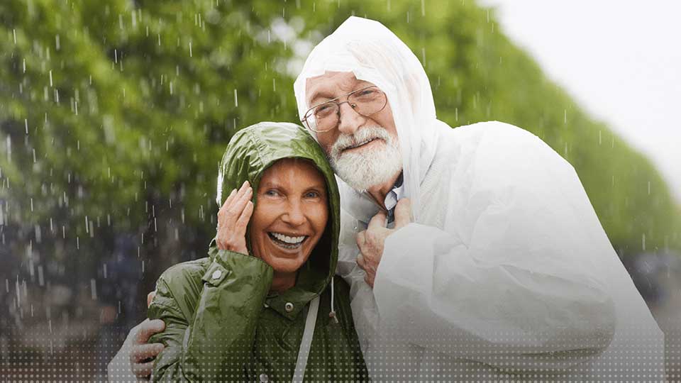 Un couple de seniors portant des aides auditives marche sous la pluie en imperméables.