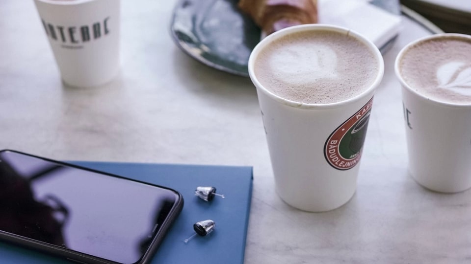 Des appareils auditifs intra-auriculaires posés sur une table avec un café et un téléphone