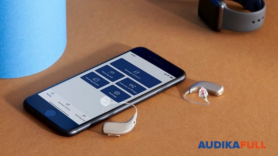 Appareils auditifs connectés placés à côté d'un smartphone affichant une application de contrôle, posés sur une surface en bois.