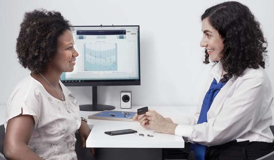 audioprothésiste expliquant un audiogramme à une patiente dans un cabinet équipé d’appareils auditifs