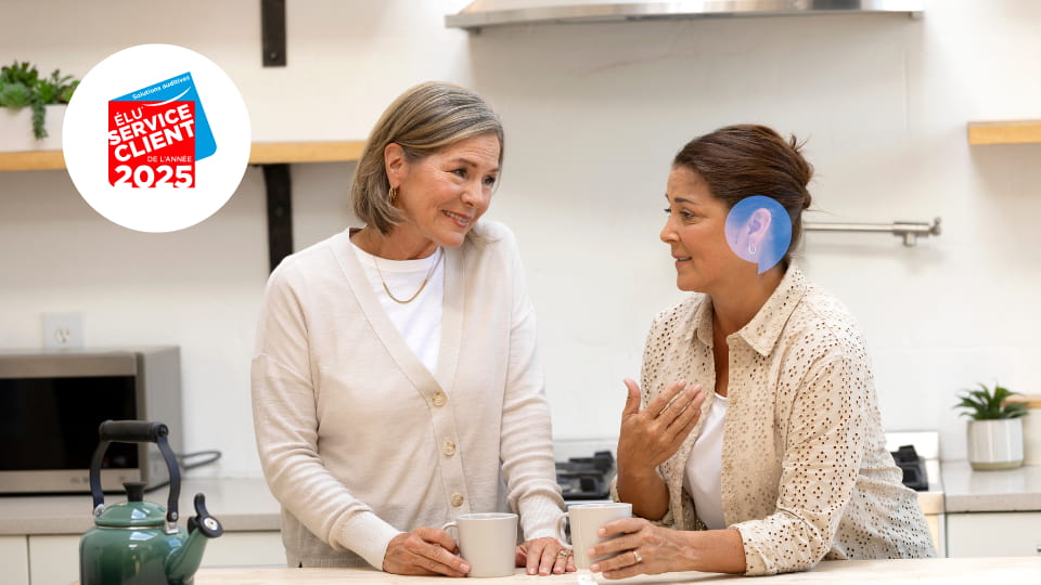Deux personnes discutant dans une cuisine, l’une portant des appareils auditifs Audika.