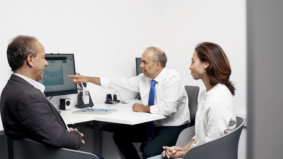 Un couple lors d’une consultation avec un audioprothésiste examinant un audiogramme sur un écran.