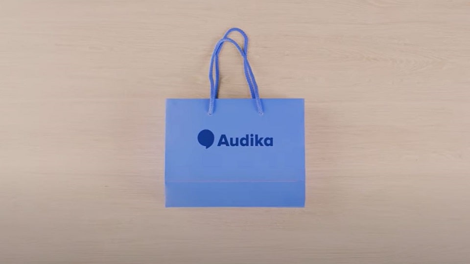 Sac cadeau bleu Audika posé sur une surface en bois, utilisé pour transporter des aides auditives.