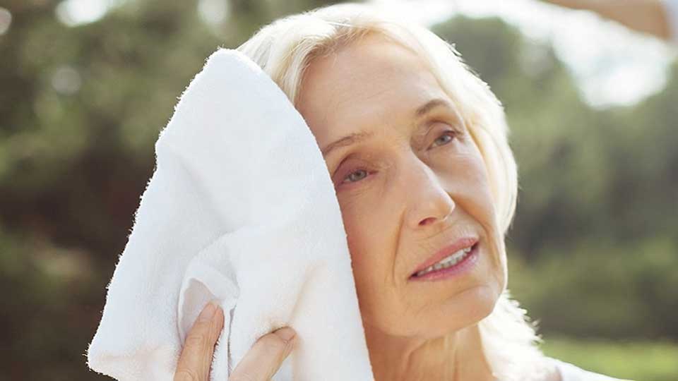 Une femme sèche ses cheveux avec une serviette blanche dans un cadre extérieur lumineux.