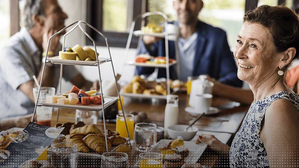 Une famille partageant un brunch avec des pâtisseries, des fruits frais et des boissons sur une table lumineuse.