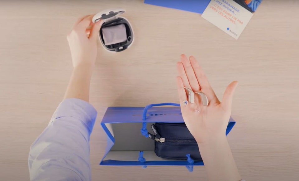 Contenu de la trousse Audika comprenant des aides auditives, un étui de rangement et un livret d’accompagnement.